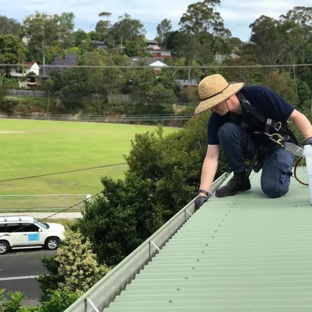 Shannan clearing gutters on a green tin roof
